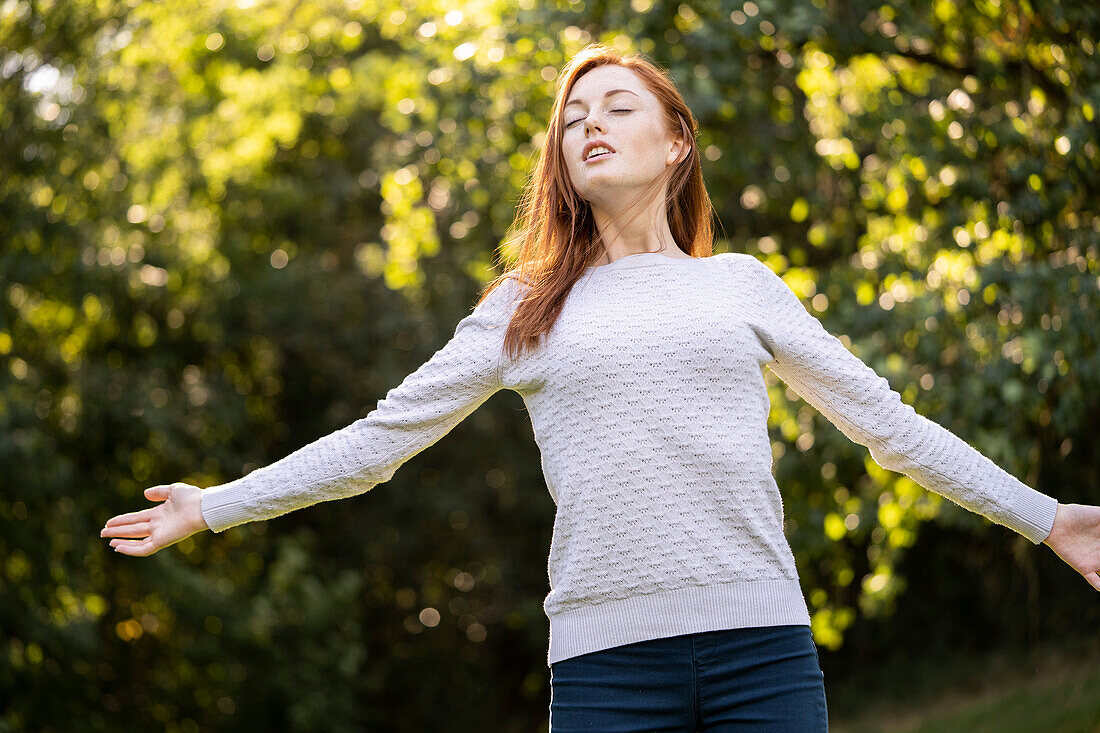 Junge Frau mit geschlossenen Augen, die ihre Arme im Park ausstreckt