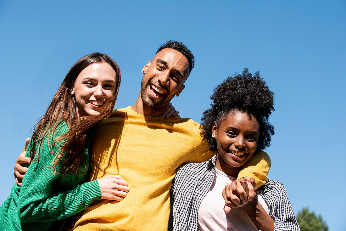 Portrait of smiling young friends standing with arm around in public park