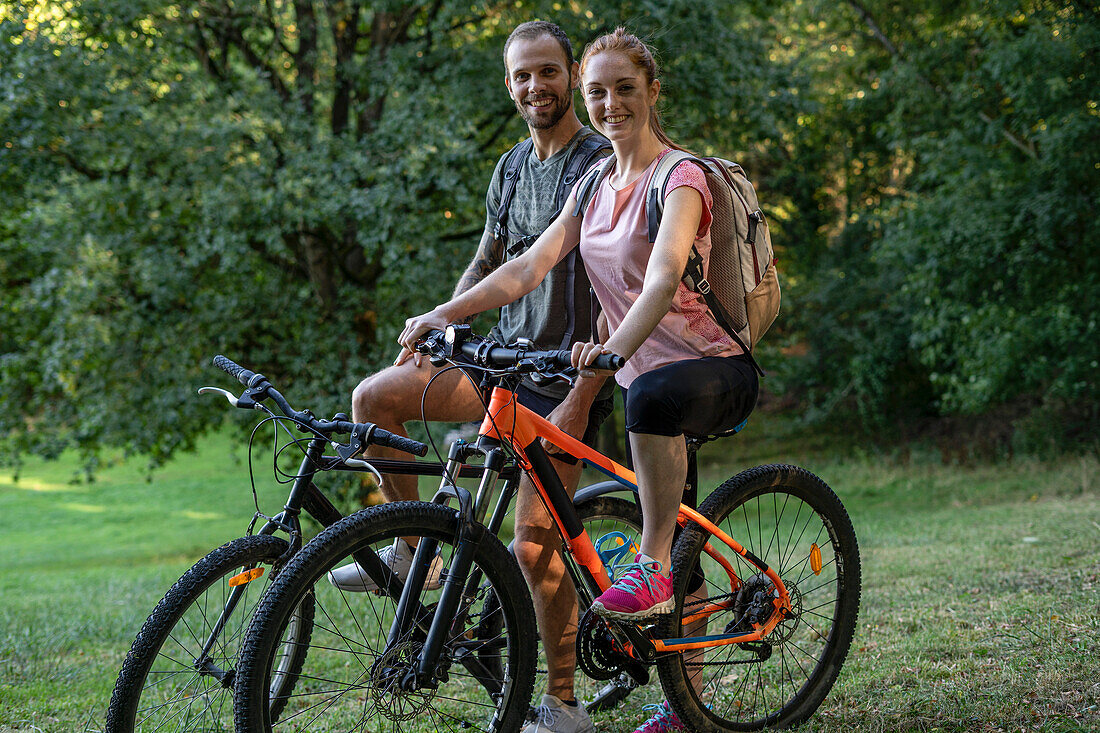 Portrait of smiling young couple sitting on bicycles in forest