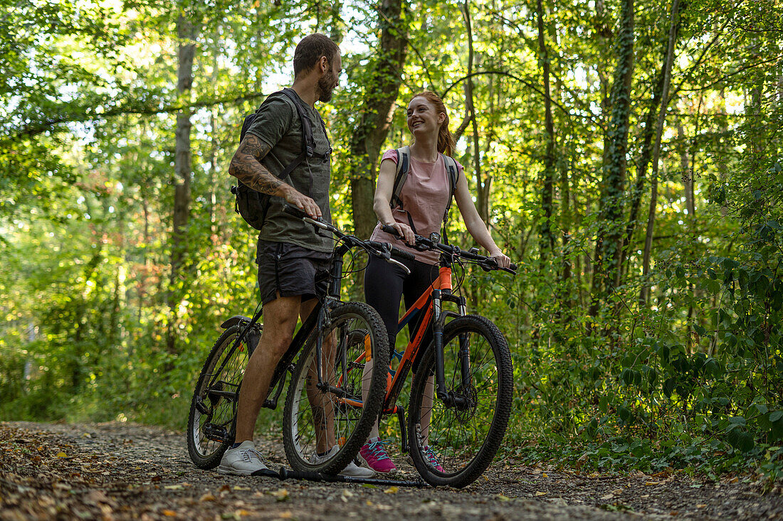 Smiling young couple standing with bicycles in forest