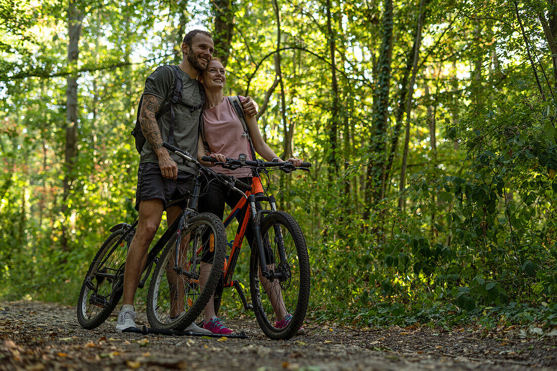 Smiling young couple standing with bicycles in forest