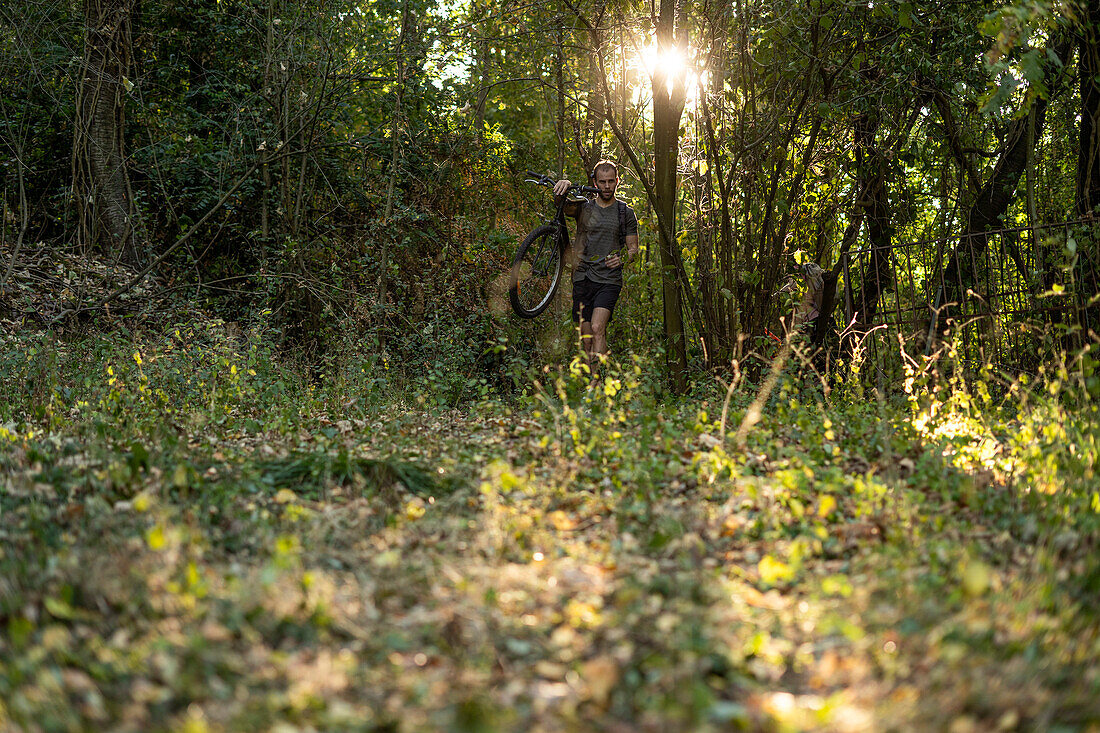 Young man carrying bicycle while walking in forest