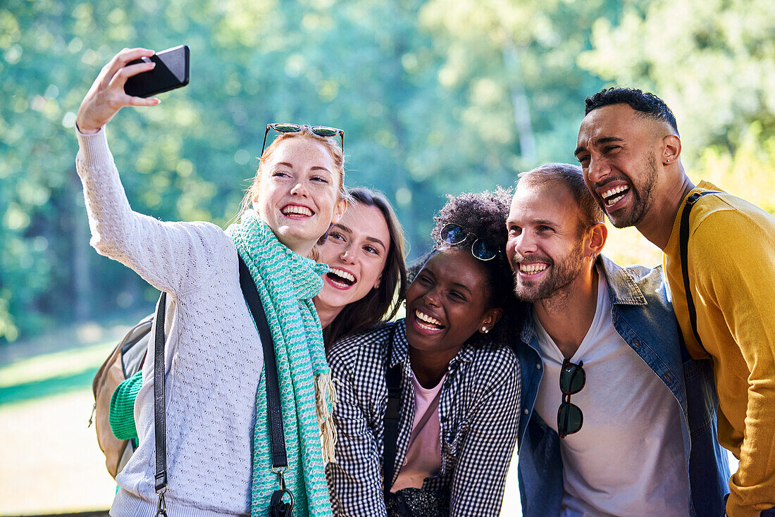 Happy friends taking selfie with smartphone in public park