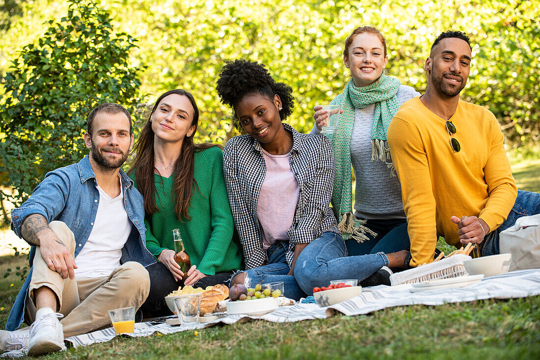 Portrait of smiling young friends having picnic in public park