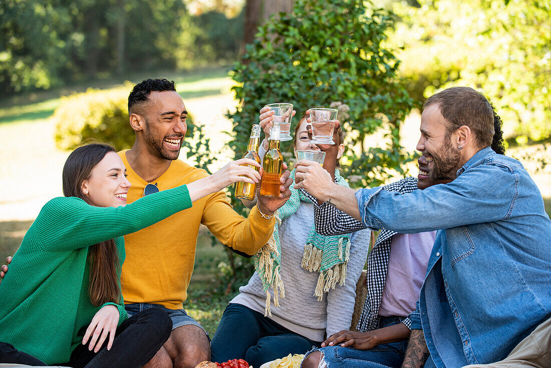 Fröhliche junge Freunde stoßen mit Getränken im Garten an