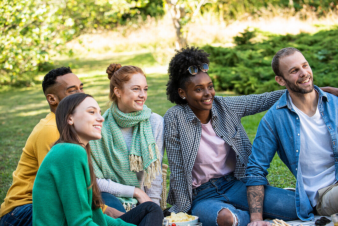 Fröhliche junge Freunde sitzen im öffentlichen Park zusammen