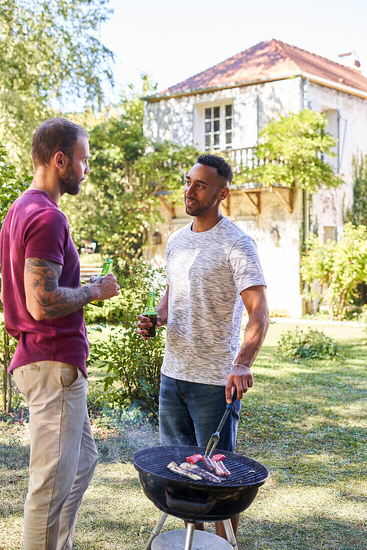 Young men with beer bottles standing near barbecue grill