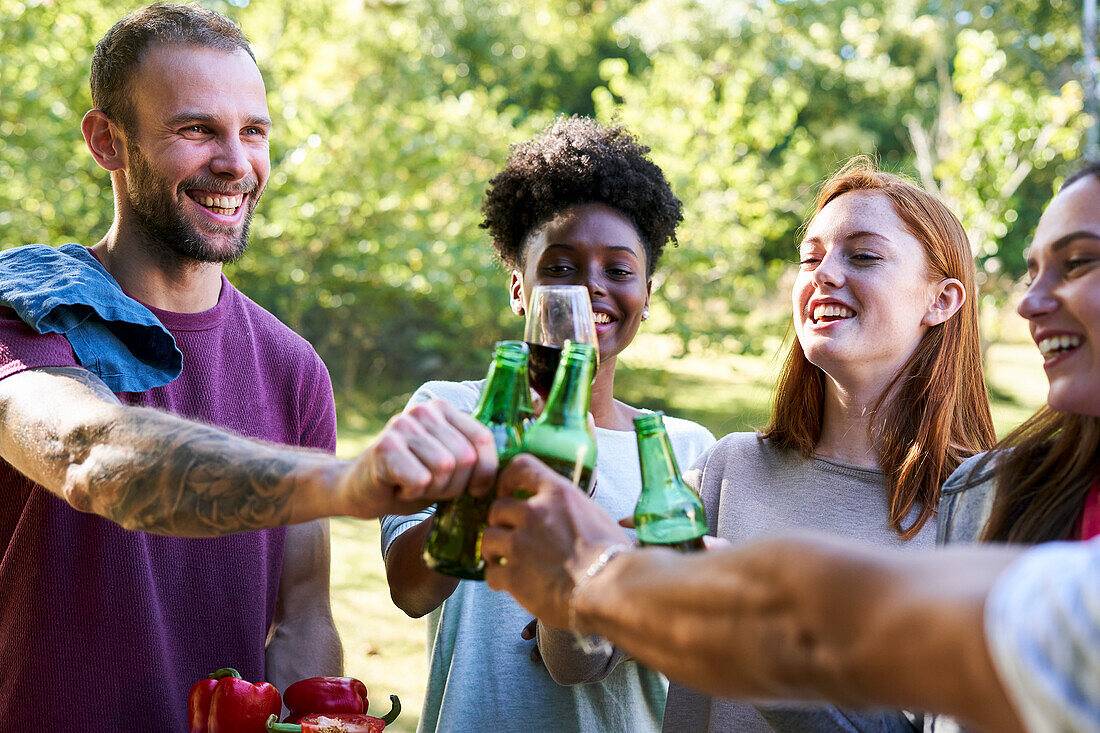 Glückliche junge Freunde stoßen mit Bierflaschen im Garten an