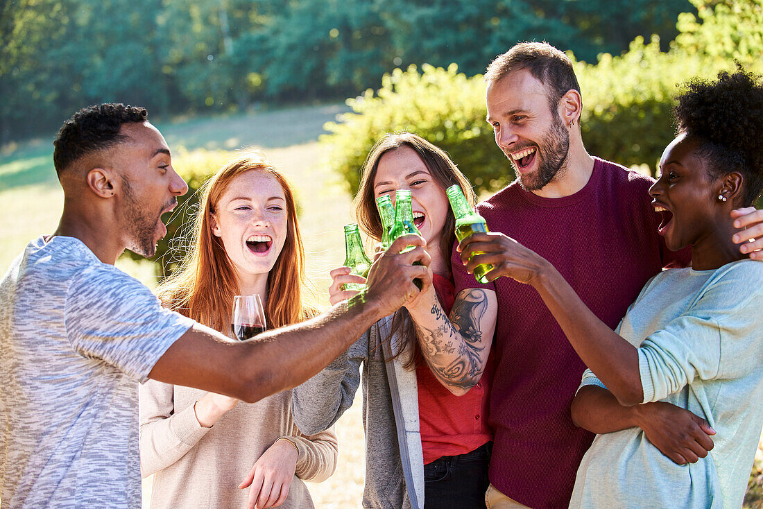 Glückliche junge Freunde stoßen mit Bierflaschen im Garten an