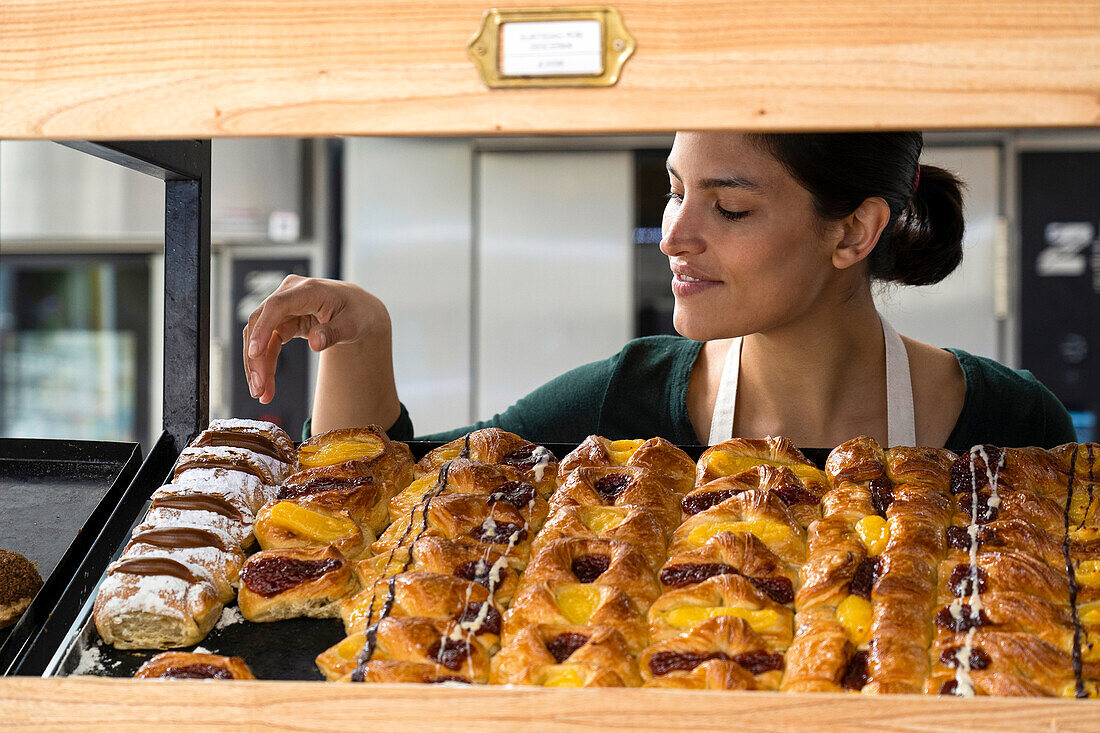 Mittlere Einstellung einer lateinamerikanischen Bäckereibesitzerin, die ihre Backwaren in einem Regal ausstellt