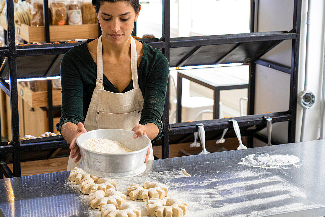 Mittlere Einstellung einer lateinamerikanischen Bäckereibesitzerin, die Mehl auf ihre Brotlaibe streut
