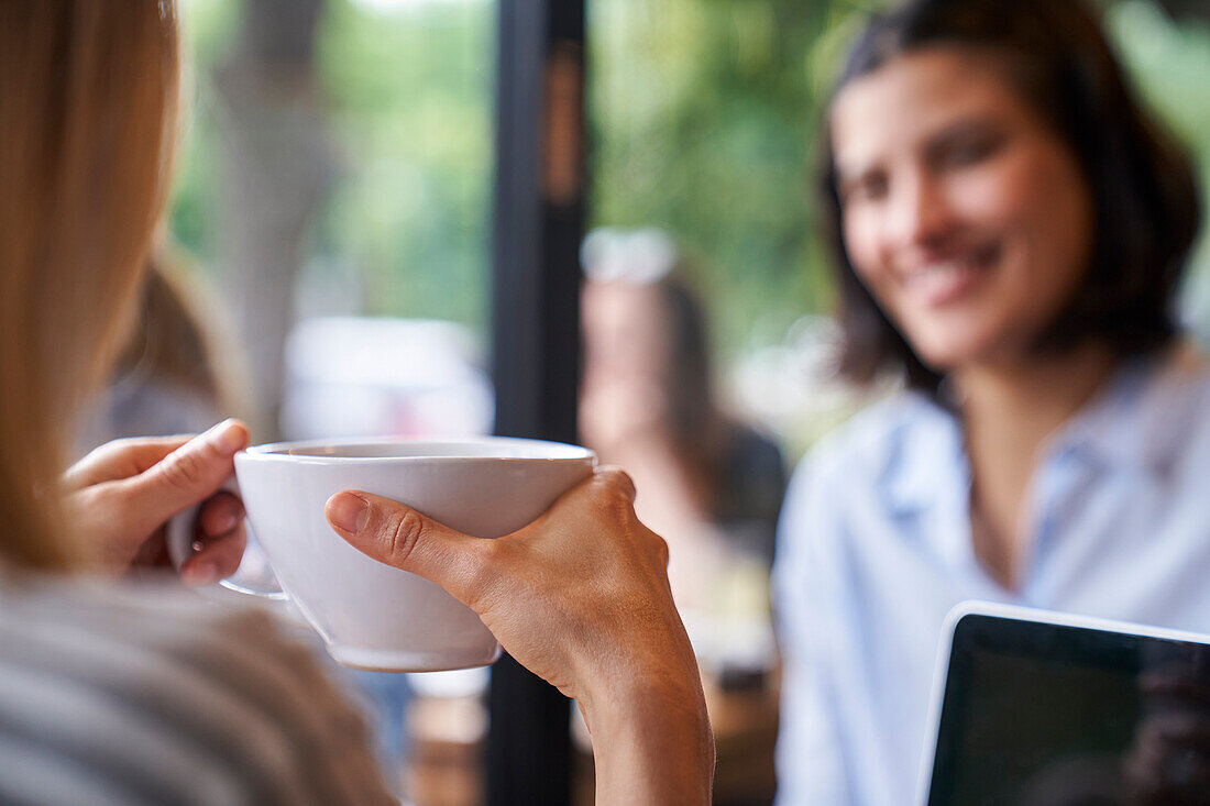 Nahaufnahme von hinten von einer Frau, die eine Tasse Kaffee in der Hand hält und sich mit einer Freundin unterhält