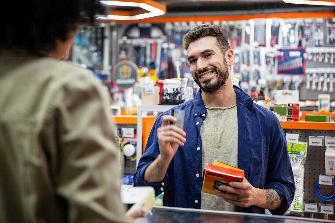 Male customer paying with credit card to African American hardware shop worker