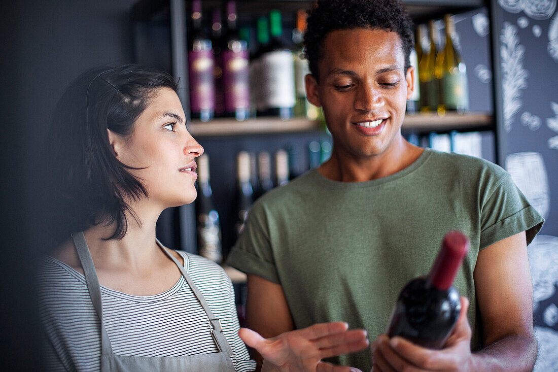 Mitarbeiterin in einem Spirituosengeschäft diskutiert mit einem Kunden über eine Weinflasche