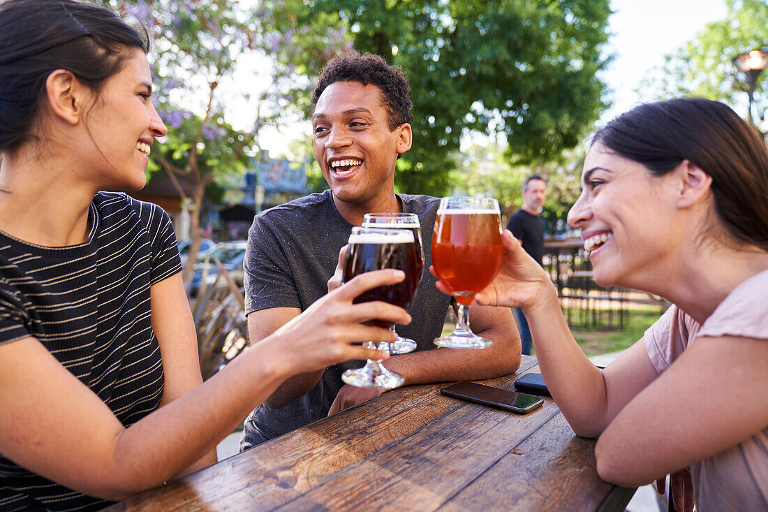 Eine Gruppe glücklicher Freunde erhebt ihre Biergläser in einer trendigen Kneipe im Freien