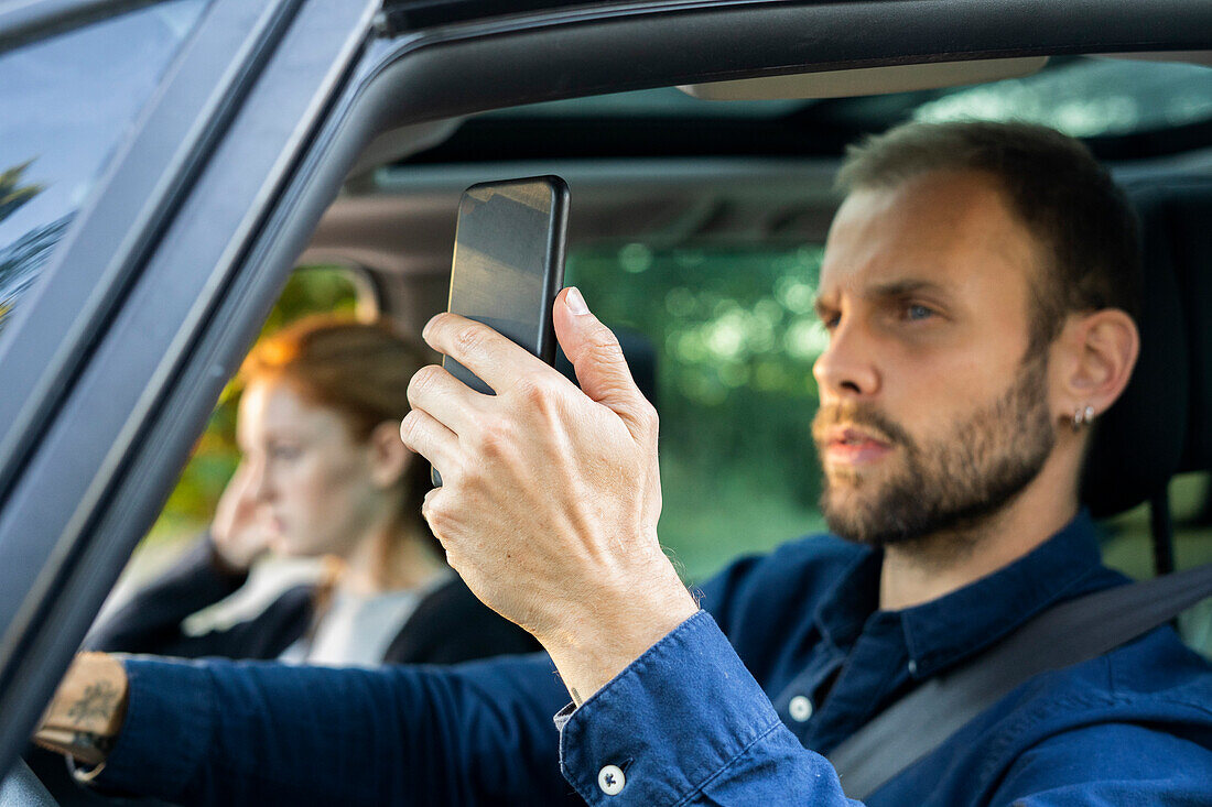 Young man using smart phone while driving a car