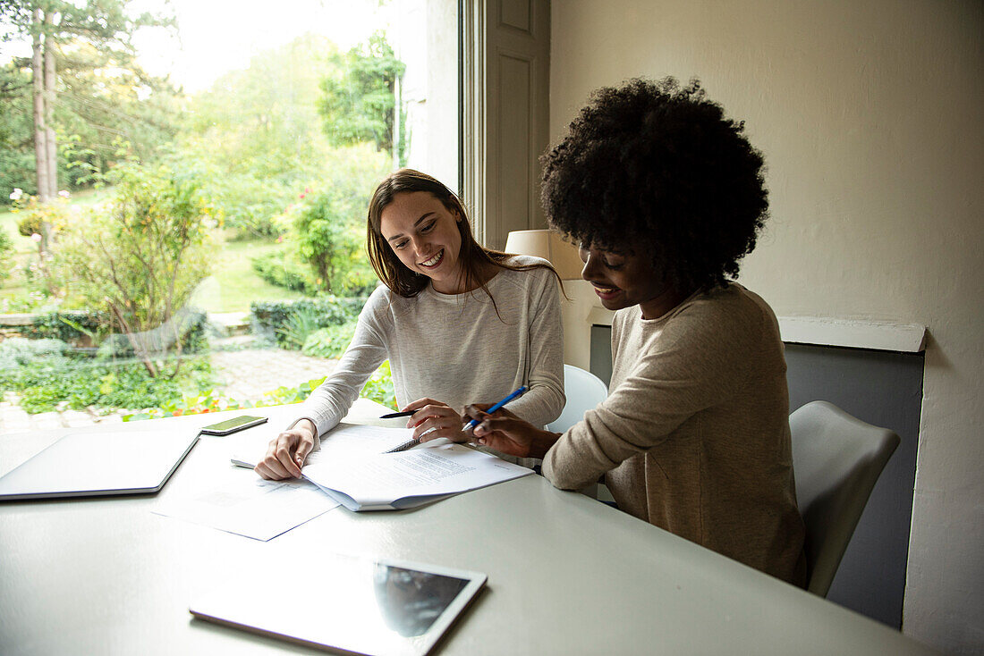 Smiling young friends writing documents together at home