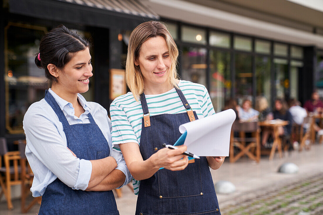 Mid-shot of two female entrepreneurs checking a list outside their restaurant