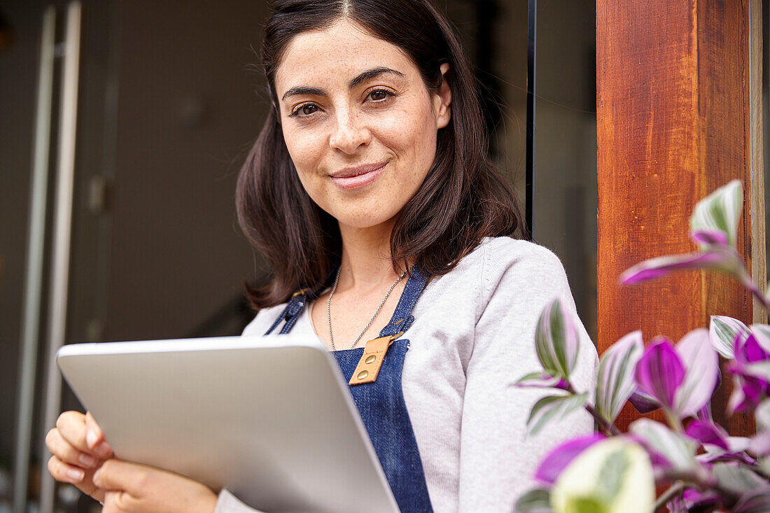 Unternehmerin schaut in die Kamera, während sie ein digitales Tablet hält