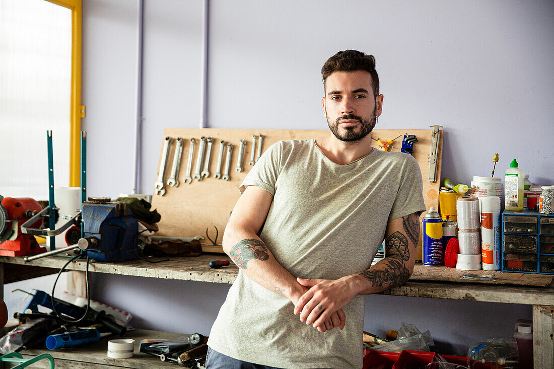 Young adult man leaning on workbench while looking at the camera