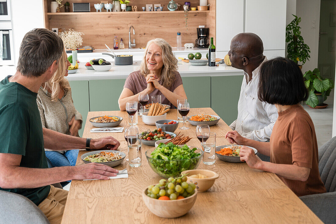 Group of diverse middle-aged friends sharing stories while having lunch at home