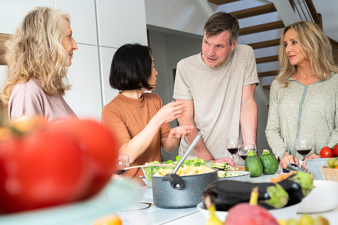 Senior Asian-American woman explaininghow to preapre a meal to group offriends while standing in kitchen