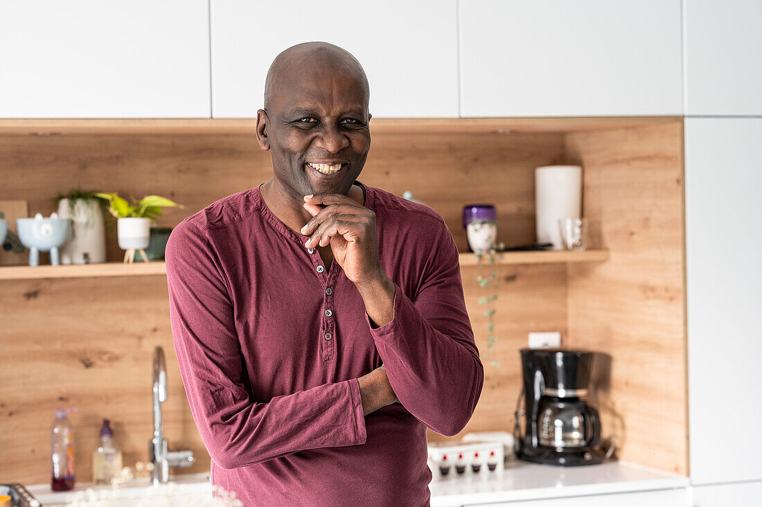 Porträt eines afroamerikanischen Mannes mittleren Alters, der in die Kamera lächelt, während er in der Küche steht