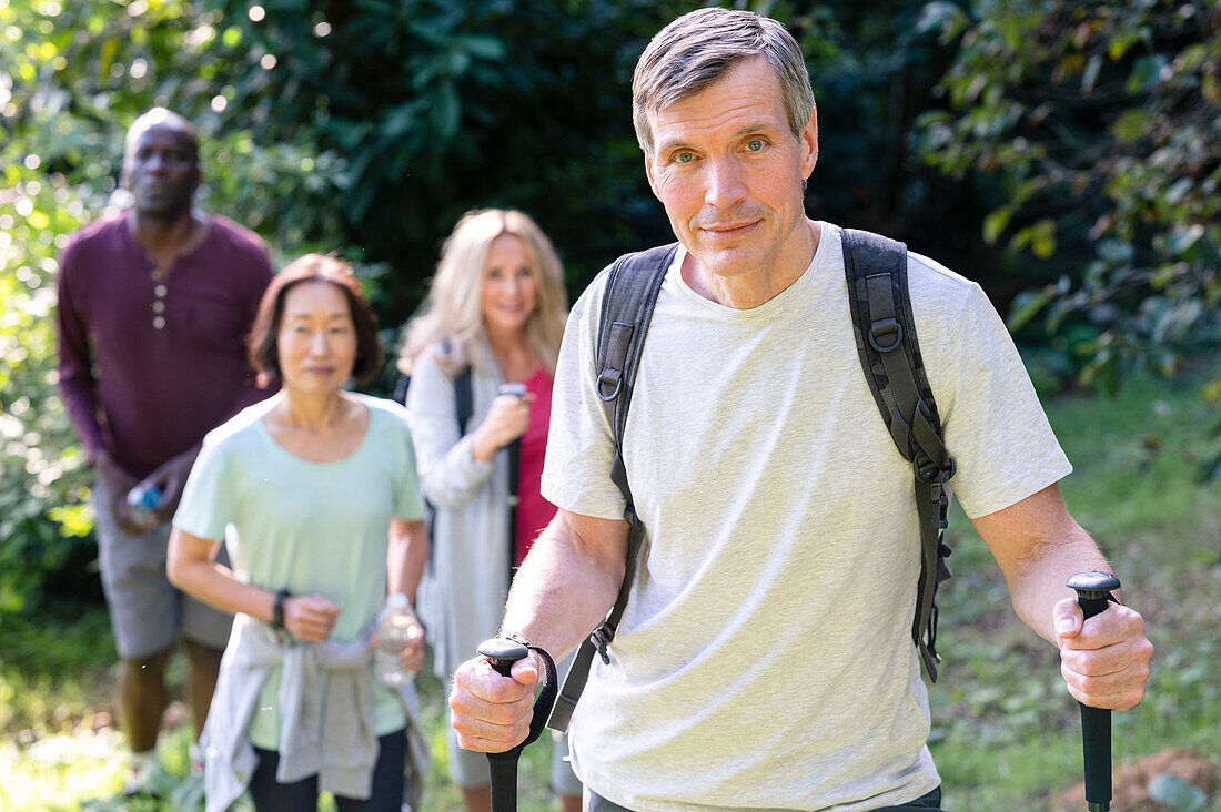 Healthy-looking middle-aged man with hiking poles and backpack hiking in the local backroads with his diverse group of friends
