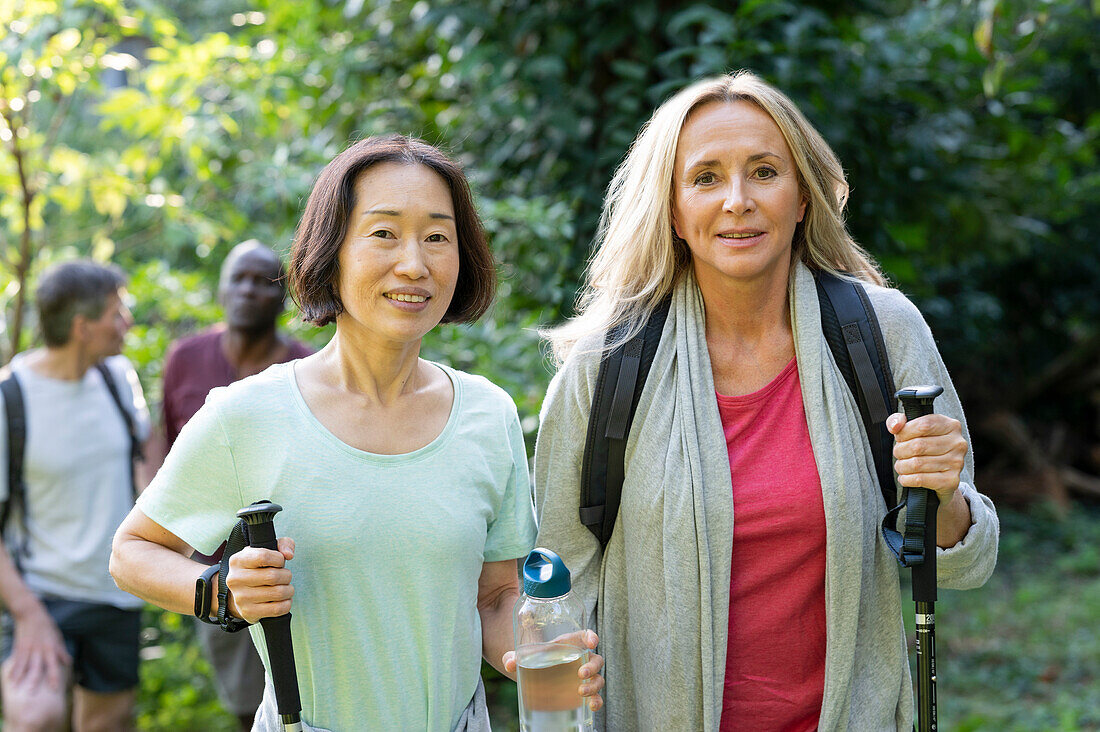 Zwei Frauen mittleren Alters mit Wanderstöcken, die mit ihren Partnern im Wald spazieren gehen