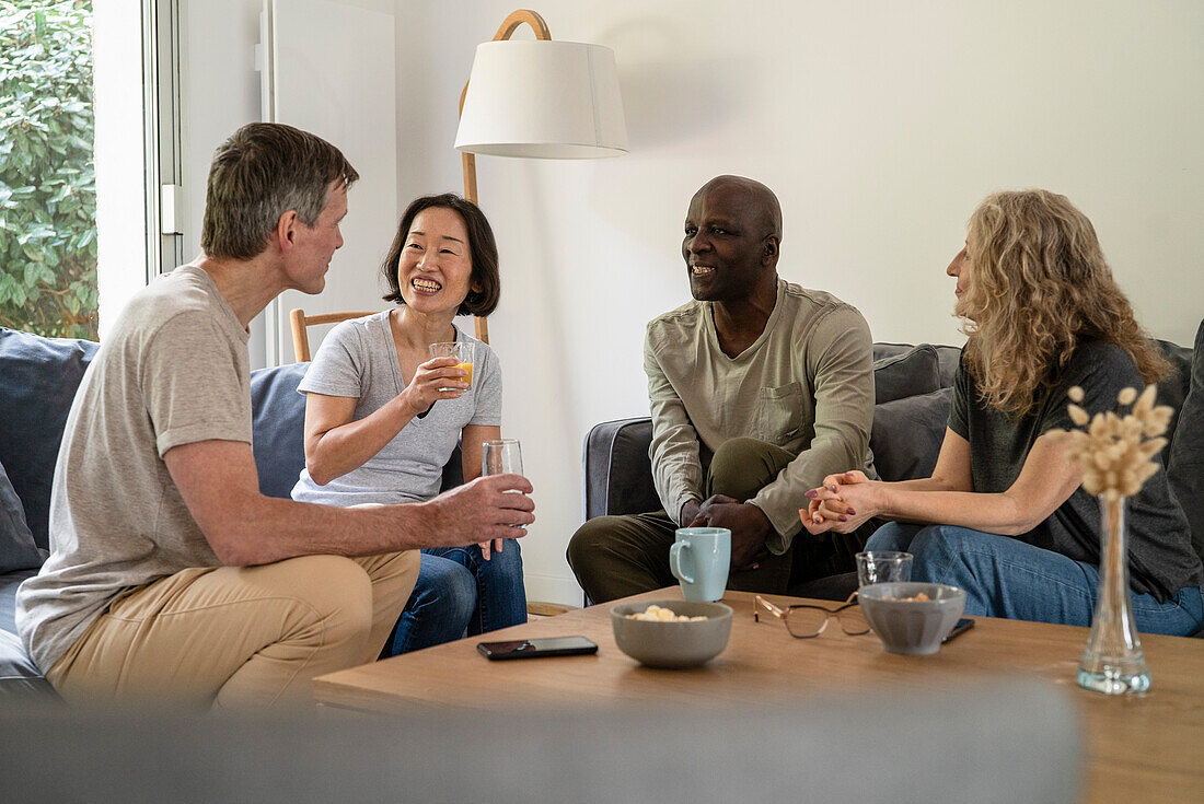 Eine Gruppe älterer Freunde sitzt auf dem Sofa und trinkt Saft und Tee