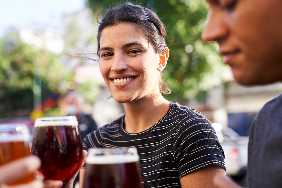 Porträt einer glücklichen jungen lateinamerikanischen Frau, die in die Kamera lächelt und ein Glas Bier in der Hand hält