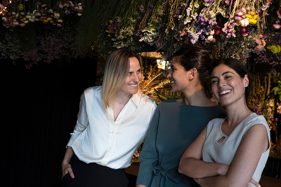 Group shot of three ethnically diverse girl friends smiling at camera while hanging out at night