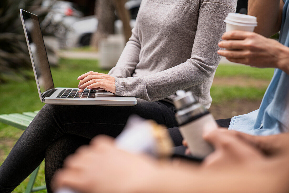 Mittelaufnahme einer Gruppe von Menschen mit Händen und einer Frau, die einen Laptop auf ihrem Schoß hält und darauf tippt