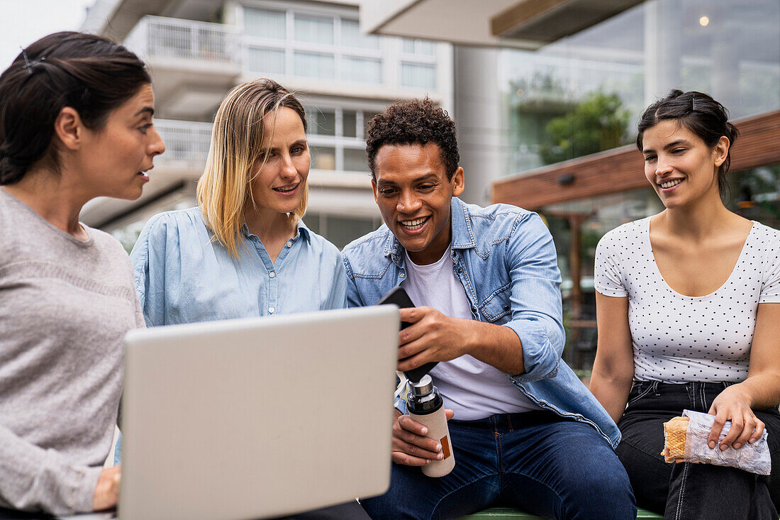 Ethnically diverse group of freelance digital nomads going over business project in outdoors settings