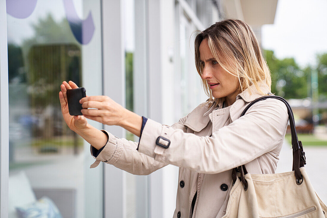 Mittlere Einstellung einer Frau, die mit ihrem Mobiltelefon ein Foto vom Schaufenster macht