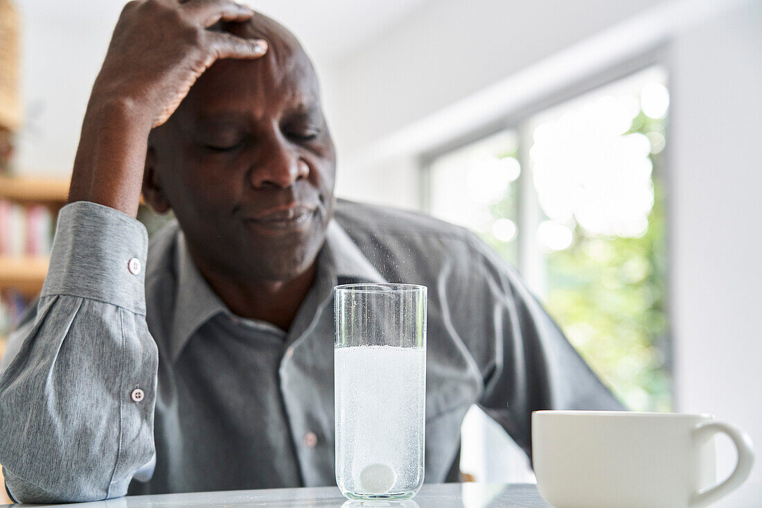 Afroamerikanischer Mann mittleren Alters mit Kopfschmerzen nimmt seine Medizin ein