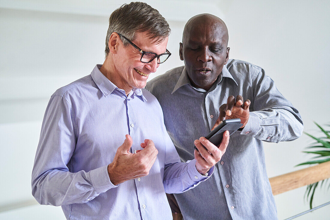 Two senior diverse male friends looking at photos on mobile phone at home