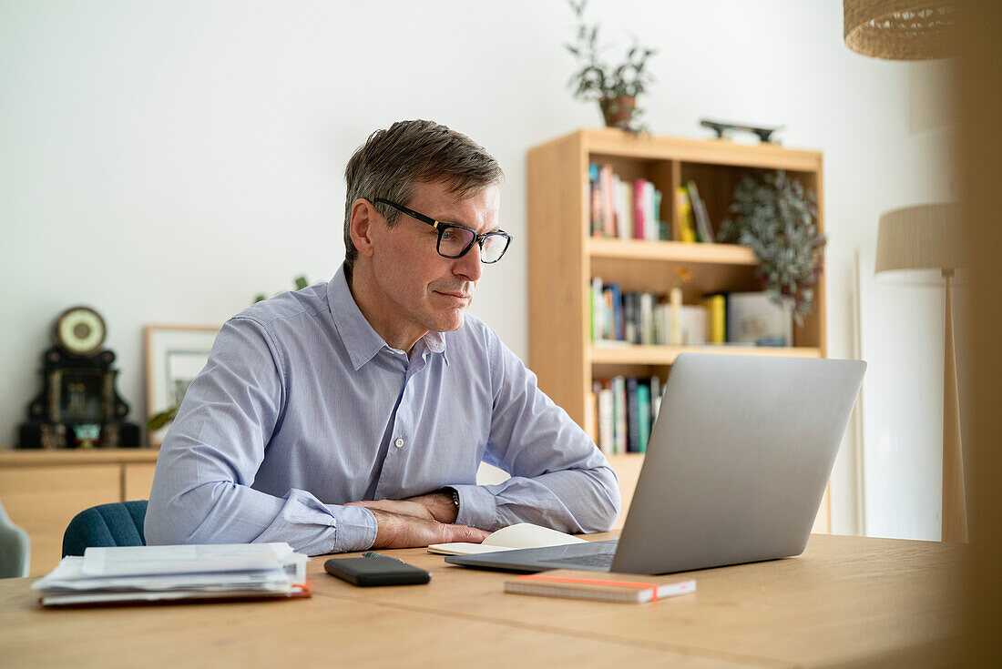 Älterer Geschäftsmann sitzt am Schreibtisch und benutzt einen Laptop