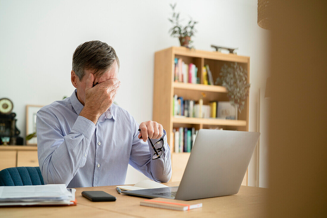 Gestresster älterer Geschäftsmann mit der Hand im Gesicht bei der Arbeit im Home Office