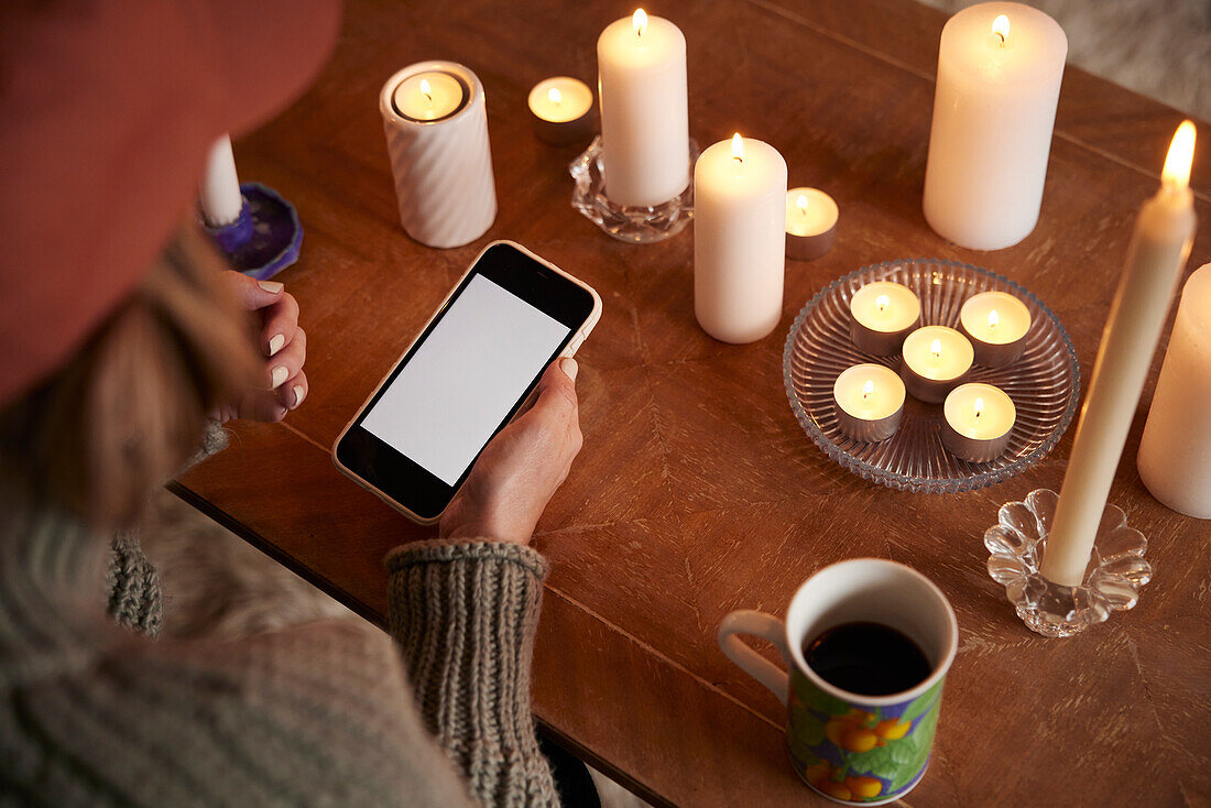 Woman using phone next to lit candles