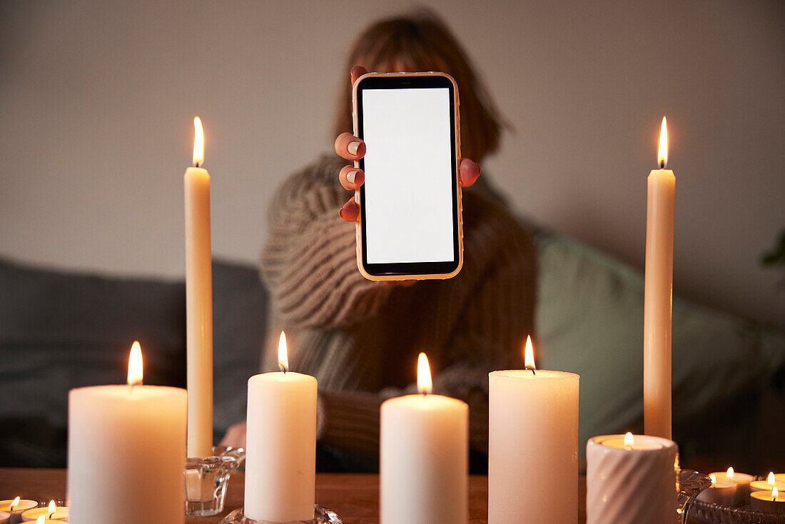 Woman showing phone over lit candles