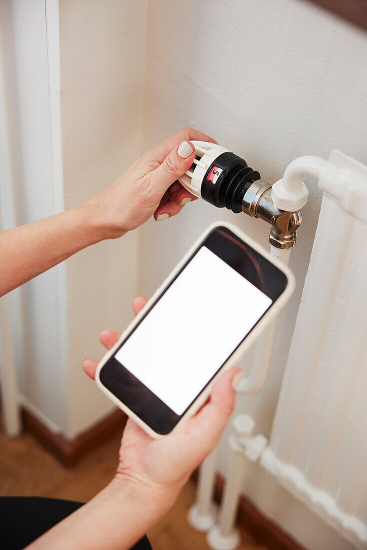 Woman holding phone and using radiator thermostat