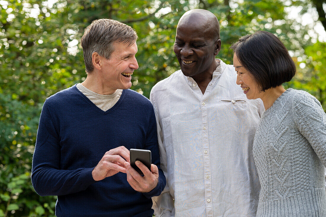 Portrait of three friends looking at cellphone's screen while hanginf out outdoors in public park