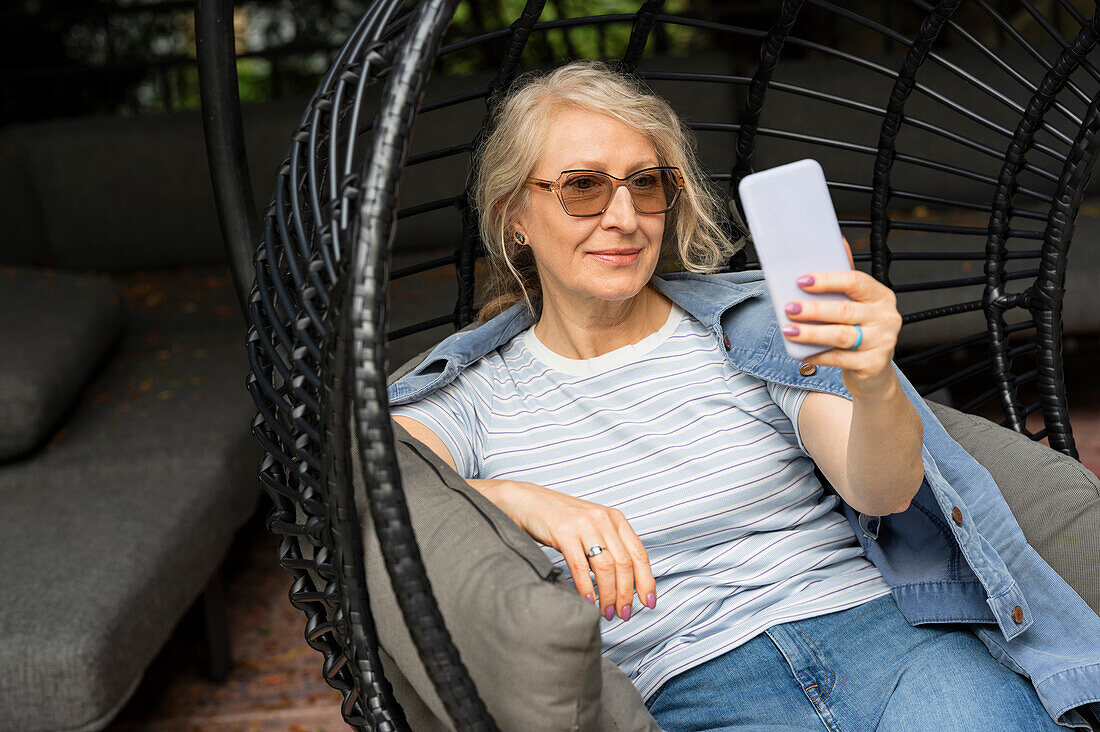 Ältere Frau, die in einem bequemen Gartenstuhl sitzt und ein Selfie macht