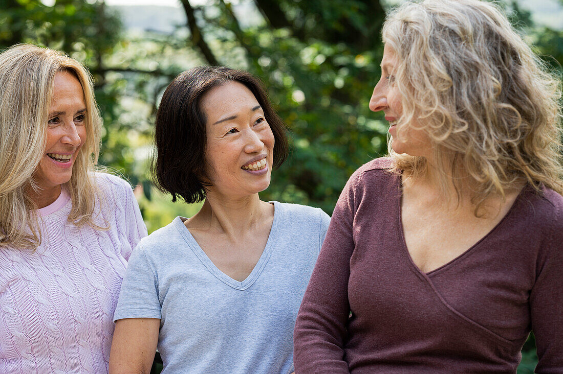 Drei Frauen mittleren Alters unterhalten sich freundlich in ihrem Garten