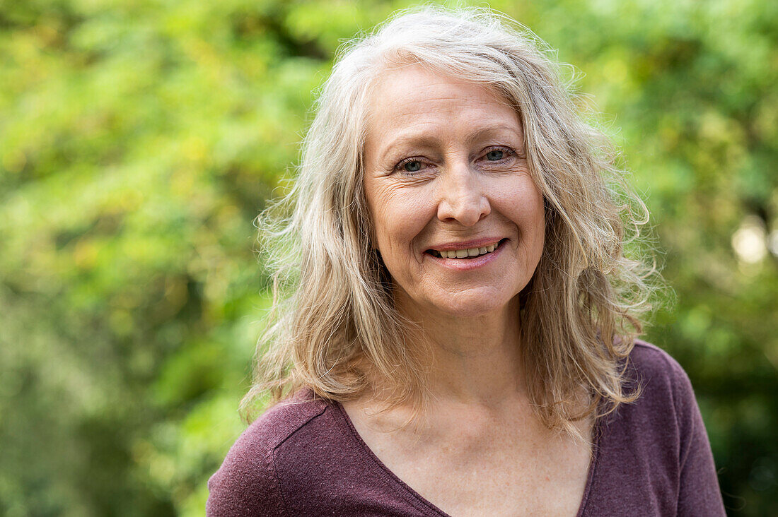 Portrait of middle-aged lady looking at camera while sitting outdoors in backyard