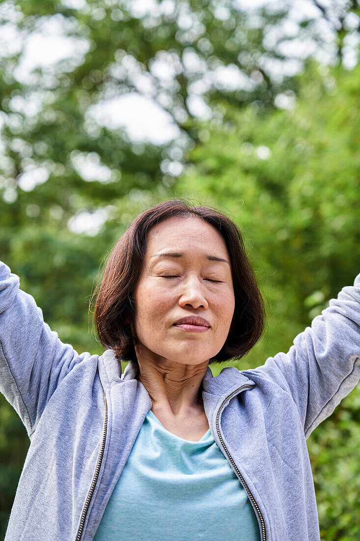 Senior Asian woman raising hands while taking a deep breath