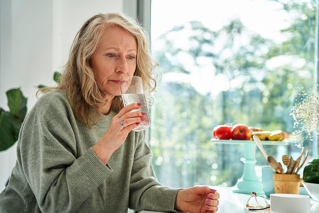Besorgte Seniorin trinkt Wasser, während sie am Tresen sitzt