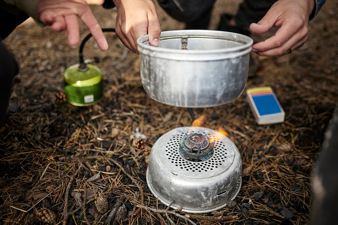 Person stellt Topf auf Campingkocher