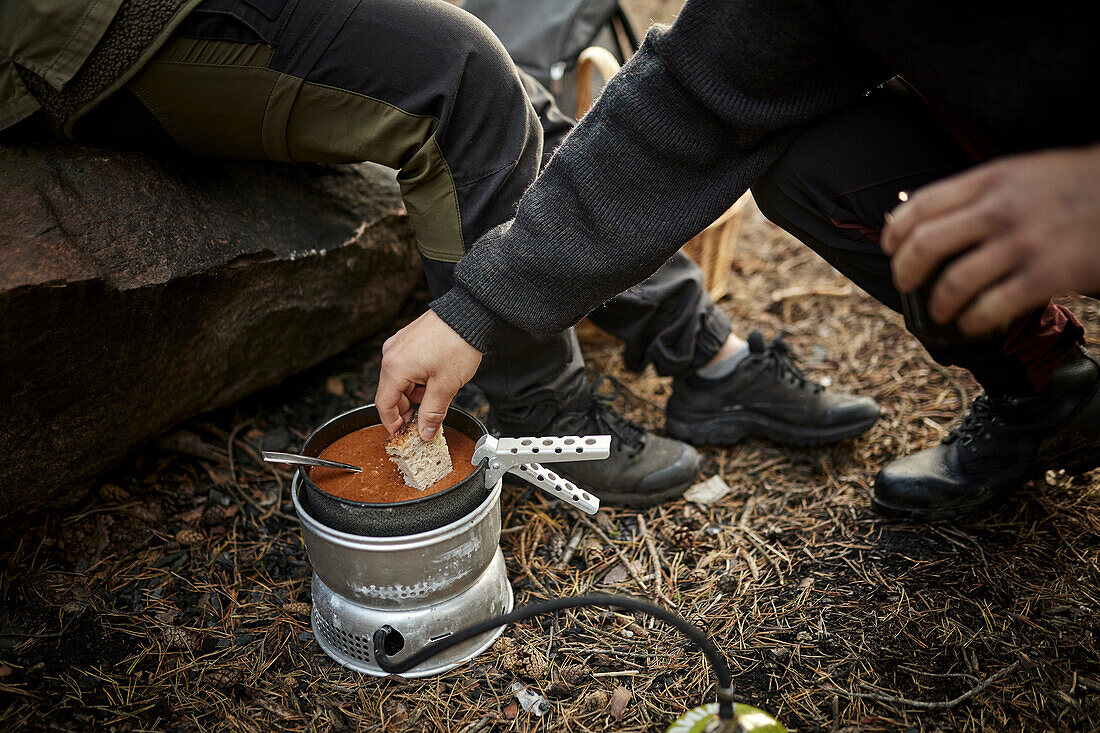 Hand legt Brot in den Topf auf dem Campingkocher